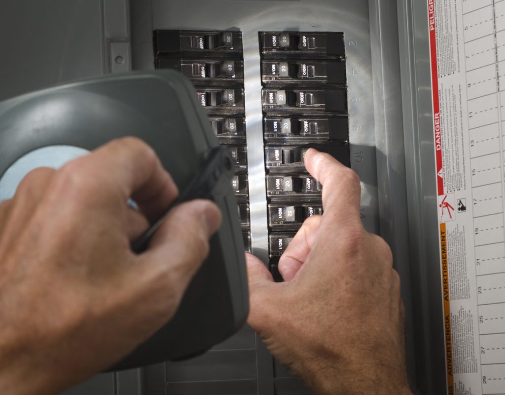Technician with flashlight at residential circuit breaker panel.