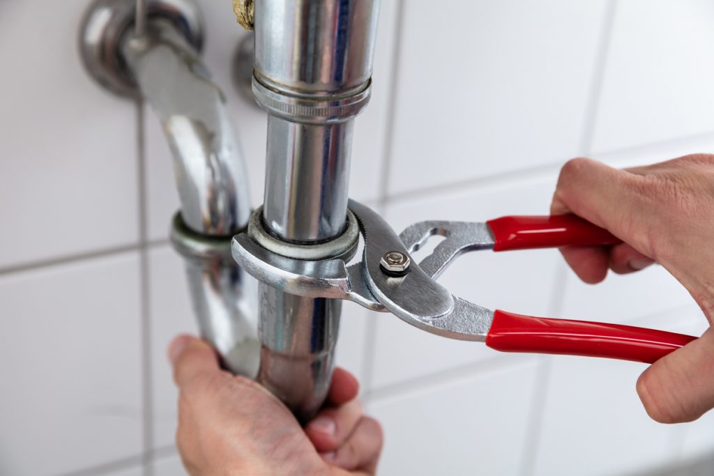 Plumber repairing sink pipe with adjustable wrench with red handles.
