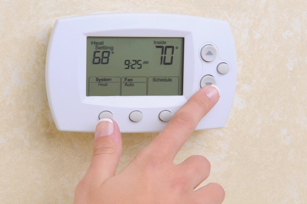 Close-up of a hand adjusting a thermostat on the wall.