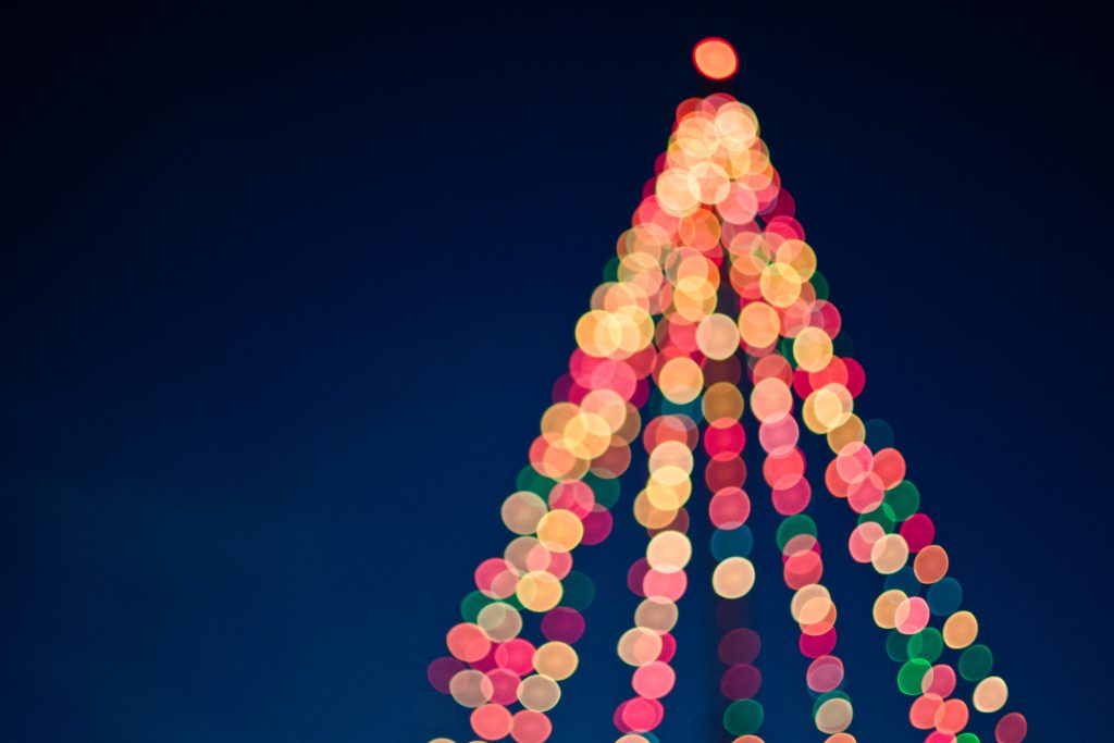 Blurry image of lights in the shape of a Christmas tree, on navy blue background.
